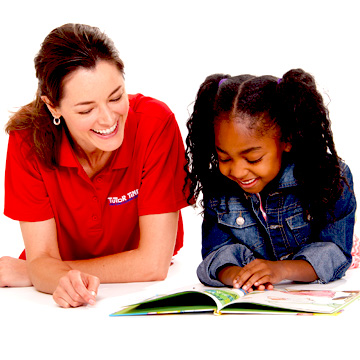 Una maestra y una niña apoyadas en el piso leyendo