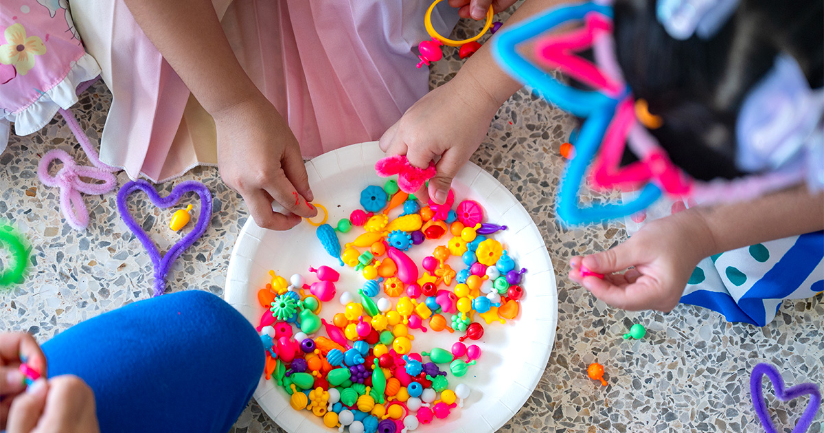 plate of beads with little girl hands over it